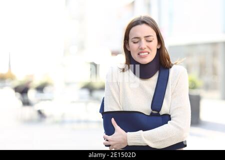 Vorderansicht Porträt einer gestressten Frau leiden mit gebrochen Arm auf einer Schlinge, die auf der Straße läuft Stockfoto