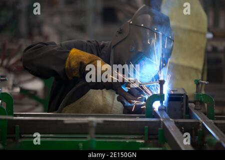 Unanstiraler Arbeiter in Maske, beim Schweißen von Metall mit hellem Licht, Rauch und Funken Stockfoto