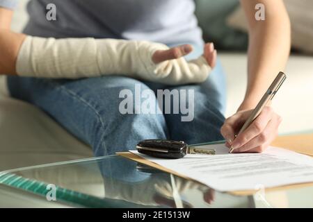 Nahaufnahme einer Dame Hände mit gebrochenem Arm Unterzeichnung Versicherungsdokument nach Autounfall zu Hause Stockfoto