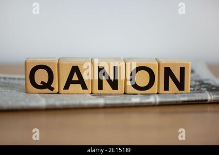 Q Anon-Symbol. Würfel auf einer Zeitung mit dem Wort 'QANON'. Schöner Holztisch. Weißer Hintergrund. Business und Q Anon Konzept. Speicherplatz kopieren. Stockfoto