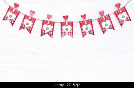 Karierte rote Fahnen mit Filzherzen auf Wäscheklammern hängen an einem Jute-Seil auf weißem Hintergrund. Happy Valentine's Day Dekor mit niedlichen Fahnen für Design Stockfoto