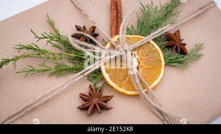 Weihnachtsgeschenk in einer schönen Verpackung aus Bastelpapier, Fichtenzweigen, Orangen- und Zimtstangen aus der Nähe. Schön eingewickeltes Geschenk in einem Scandinavi Stockfoto