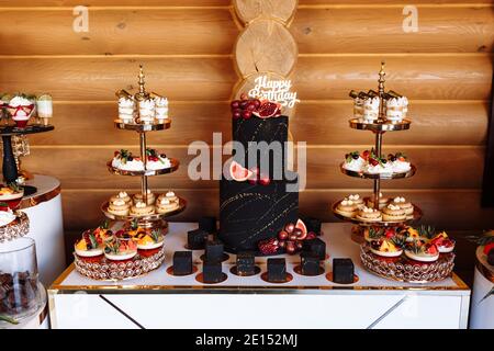 Große schwarze Geburtstagstorte mit frischem Obst und Süßigkeiten auf einem festlichen Tisch. Süßigkeitenbar. Tisch mit verschiedenen Süßigkeiten für Party. Stockfoto