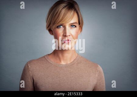 Studio-Porträt der schönen blonden behaarten Frau Blick auf die Kamera, während auf isolierten grauen Hintergrund stehen. Stockfoto