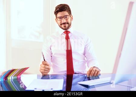 Portrait von Investment Advisor Geschäftsmann im Büro Schreibtisch saßen und an der Kamera während der Arbeit am Computer. Stockfoto
