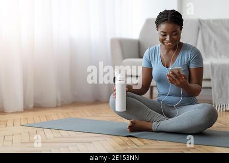 Schwarze Dame Entspannt Mit Smartphone Auf Yoga-Matte Nach Dem Training Zu Hause Stockfoto