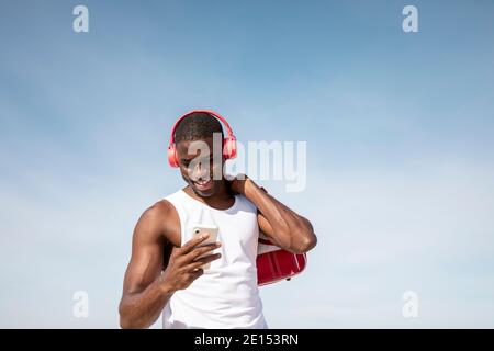 Junger schwarzer Sportler lacht, während er Musik auf seinem Handy hört. Junger Mann lacht beim Plaudern. Stockfoto