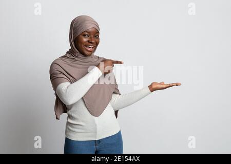 Aktivieren Sie Diese Option. Aufgeregt Schwarze Frau In Hijab Zeigt Auf Ihre Leere Handfläche Stockfoto