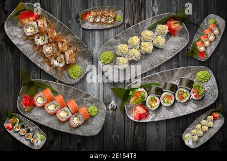 Verschiedene Sushi-Rollen auf den Tellern verschiedener Größen, die Collage, auf dem grauen Brett Stockfoto