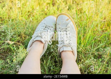 Nahaufnahme der weiblichen Füße in weißen Sneakers im grünen Gras Der Sommerwiese Stockfoto