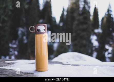 Gelbe Thermoskannen auf Holztisch im Winter im Freien. Stockfoto