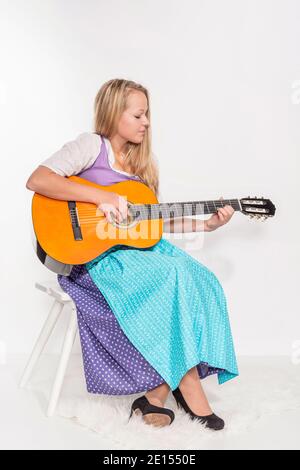 Junge Frau in Dirndl Kleid sitzt auf EINEM Hocker und Spielt Die Gitarre Stockfoto