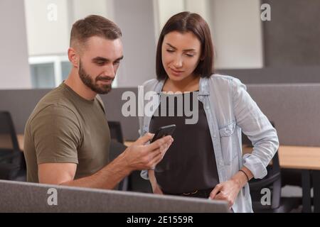 Attraktive Geschäftsfrau und ihre männlichen Kollegen beobachten etwas auf einem Smartphone Stockfoto