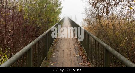 Blick auf einen hölzernen Steg mit festem Geländer auf beiden Seiten. Ins Unbekannte führen. Neblige Luft in der Ferne. Stockfoto