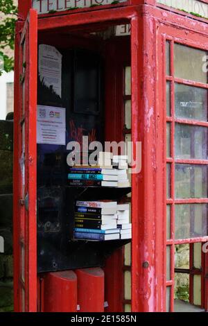 Ein verlassener Kiosk mit roten Telefonen ist zu einer temporären Bibliothek geworden, in der Menschen Bücher ausleihen können, Harrogate, North Yorkshire, Großbritannien. Stockfoto