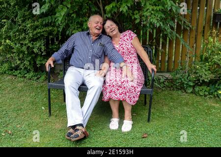 Ein lachendes Seniorenpaar, das auf einer Bank im Garten sitzt. Seniorenpaar glücklich Stockfoto
