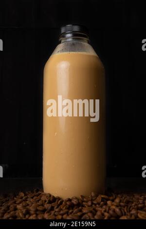 Eine Flasche Kaffee Latte in dunklem Hintergrund. Später Kaffee wird in das Glas gegossen Stockfoto