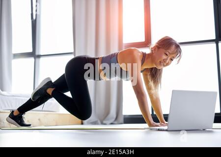 Frau genießen Training auf Matte allein zu Hause, geben Online-Bildungs-Pilates-Workshop, mit Laptop. Starke Frau in Sportswear Stockfoto