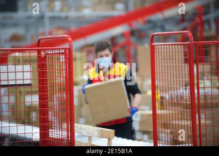 Ein Arbeiter mit Schutzmaske, der eine Kiste in der Logistik bewegt Zentrieren Stockfoto