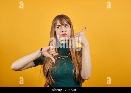 Menschliche Hand Daumen nach unten, kein okay Zeichen, wütend Gesicht, negative Geste zeigt Abneigung mit Finger, Ablehnung. Junge attraktive Frau, gekleidet grün Hemd blonde Haare, gelber Hintergrund Stockfoto