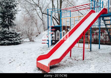 Verschneite Babyschaukel im Winter - leerer Spielplatz - Roter Plastikschaukelstuhl in der Kälte Stockfoto