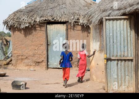 Gambische Dorfkinder laufen an Schlammhütten in der Nähe eines abgelegenen Dorfes in der Nähe von Panchang in Gambia vorbei. Stockfoto