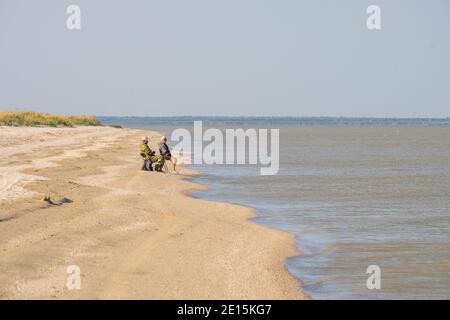 Region Krasnodar. Russland. Juli 26, 2020. Zwei Fischer mit Angelruten am Nachmittag an der sandigen Küste. Ein Mann und eine Frau fischen Stockfoto