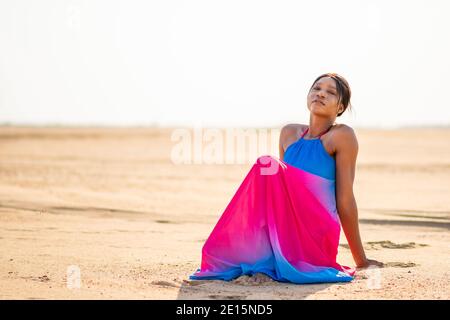 Schöne afrikanische Frau trägt ein buntes Kleid sitzt auf dem Sand am Strand, Urlaubskonzept Stockfoto