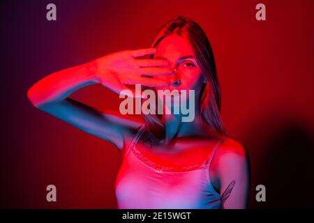 Unemotional junge Frau, die Augen mit der Hand im Studio mit bedeckt Rotes Licht Stockfoto