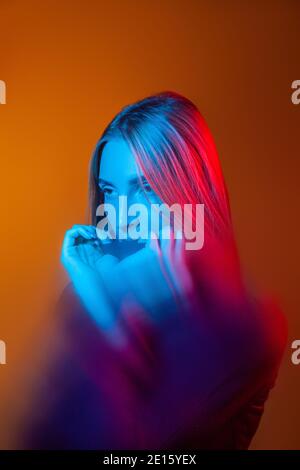 Nachdenkliche junge Dame mit blauem Licht im Gesicht in orange studio Stockfoto