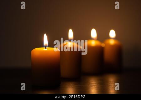 Eine Reihe brennender Kerzen, die in der Dunkelheit brennen. Goldene Töne mit selektivem Fokus auf Kerze und Hintergrundunschärfe Stockfoto