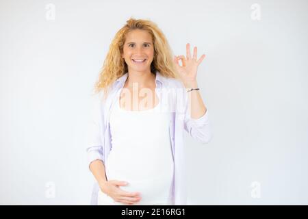 Schöne Frau erwartet ein Baby, berühren schwangeren Bauch lächelnd positive tun okay Zeichen mit Hand und Fingern. Erfolgreicher Ausdruck. Stockfoto
