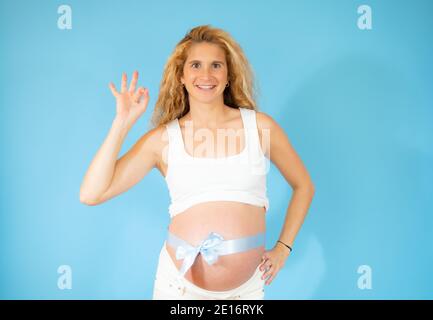 Schöne Frau erwartet ein Baby, berühren schwangeren Bauch lächelnd positive tun okay Zeichen mit Hand und Fingern. Erfolgreicher Ausdruck. Stockfoto