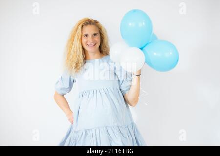 Freudige und schwangere Frau in blauem Kleid hält Ballons isoliert Auf Weiß Stockfoto