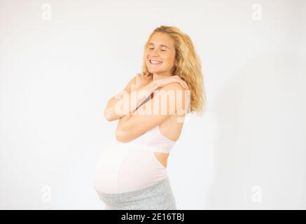 Junge schöne Frau schwanger erwartet Baby umarmt sich glücklich und positiv, lächelnd zuversichtlich. Selbstliebe und Selbstversorgung Stockfoto