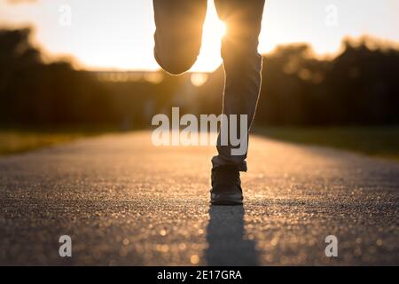 Nahaufnahme der Mannbeine, die bei Sonnenuntergang laufen. Mann läuft Joggen auf Stadtpark Straße Stockfoto