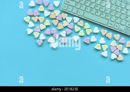 Bunte herzförmige Bonbons und Tastatur auf türkisfarbenem Hintergrund. Valentinstag, Konzept der Liebe. Draufsicht, flach liegend, Kopierbereich. Stockfoto