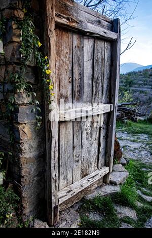 Alte Holztür teilweise von einem Dorfhaus mit geöffnet Kleine gelbe Blüten auf einer Seite und ein Blick auf Die Landschaft im Hintergrund Stockfoto