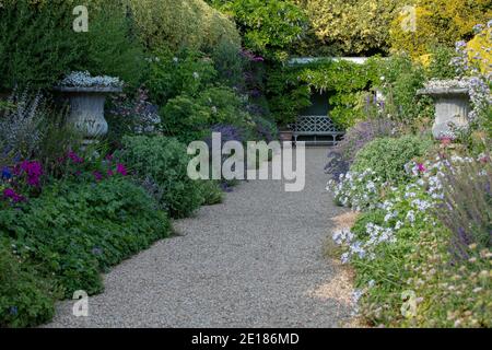 Krautige Grenzen mit permanenten Pflanzen auf beiden Seiten eines Kiesweges zu einem Gartensitz in Ascott House, Großbritannien gesehen. Stockfoto