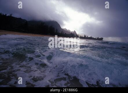 Wellen im Wildwasser an einem bewölkten Tag am Haena Beach, North Shore von Kauai mit Bali-Hai-Gipfeln im Hintergrund. Stockfoto