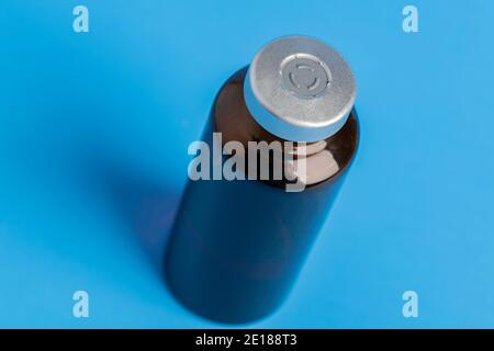 Eine Makroaufnahme mit selektivem Fokus auf einer bernsteinfarbenen Impfstoffflasche auf einem klaren blauen Hintergrund. Stockfoto