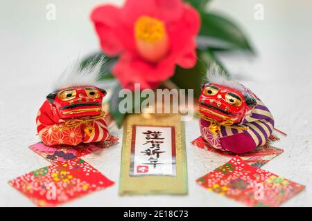 Japanische Neujahrskarte mit handschriftlichen Ideogrammen Kingashinnen oder Happy Neujahr und zwei Shishi Löwen gegen eine tsubaki Kamelie Blume im Hintergrund Stockfoto