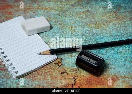 Notizbuch, schwarzer Graphitstift und Radierer auf einer rustikalen Metalloberfläche. Platz zum Schreiben. Notizen Schreibkonzept. Stockfoto