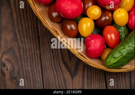 Grüne Gurken, reife Radieschen und bunte Tomaten in einem Weidenkorb Stockfoto