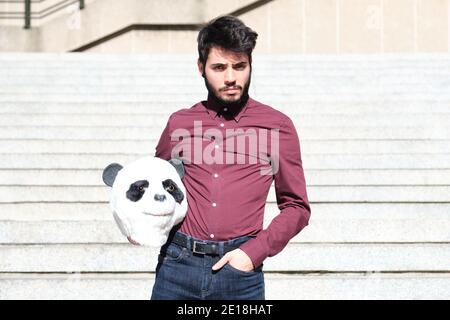 Junger Geschäftsmann mit Panda-Kopfmaske in den Händen, auf Treppen stehend. Bizarrer Geschäftsmann. Stockfoto