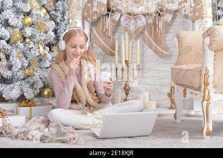 Mädchen mit Laptop Musik in der Nähe von Weihnachtsbaum hören Stockfoto