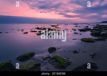 Farbenprächtiger Sonnenaufgang an der felsigen Küste des Meeres, lange Belichtung Stockfoto