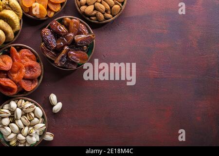 Kleine Teller mit getrockneten Früchten (Dattelpalmen, getrocknete Aprikosen, Feigen) und Nüssen (Pistazien, Mandeln) für Iftar im Ramadan auf dem dunkelroten Holzbac Stockfoto