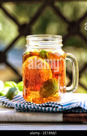 Das Glas Eistee auf Holztisch. Cuba Libre oder Long Island Cocktail, kaltes Getränk oder Limonade mit Zitrone und Basilikum. Balkon auf dem Hinterhof Stockfoto