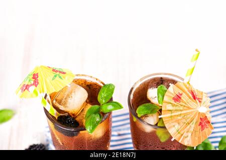 Das Glas Eistee mit Brombeere auf Holztisch. Cuba Libre oder Long Island Cocktail, kaltes Getränk oder Limonade mit Zitrone und Basilikum. Stockfoto